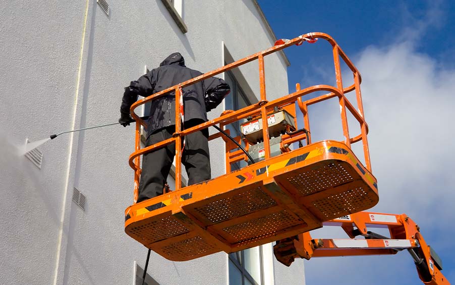 Worker prssure washing a business exterior with lift
